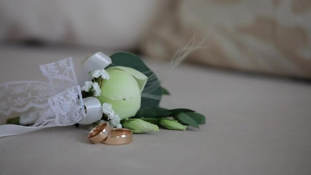 Buttonhole with white rose and wedding gold rings staying on chair prepared for bride and groom.