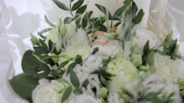 Wedding rings staying on beautiful modern bridal bouquet of fresh roses and green eucalyptus.