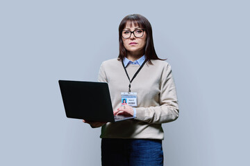 Middle aged confident serious female teacher using laptop on grey background