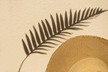 Top view of summer sun-colored abstract palm leaf shadow on the wall with beach straw hat. Minimal...