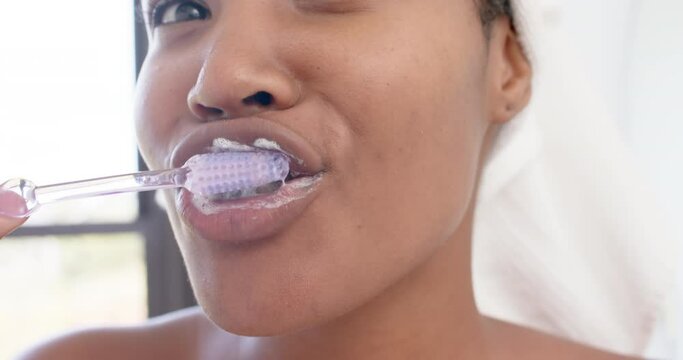 Portrait of happy biracial woman with towel on head brushing teeth, slow motion