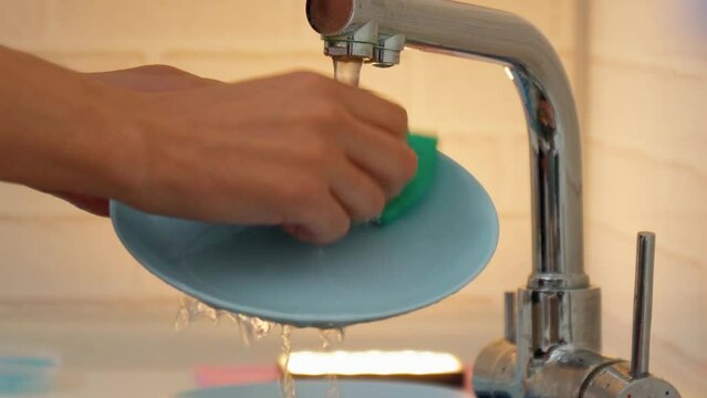 Man hands while scrubbing a dish with a scouring pad and soap and water in the kitchen.