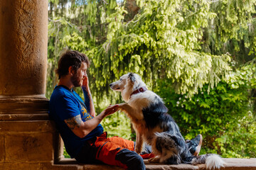 young Caucasian man enjoys playing with his border collie dog sitting in an old building....