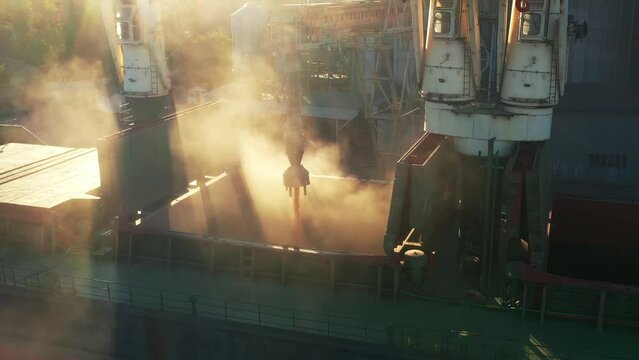 Aerial of wheat loading to bulker ship cargo hold at sea grain elevator in sea port. Wheat pouring from silo to bulk vessel via trunk at sea port terminal. Transportation of agricultural commodities.