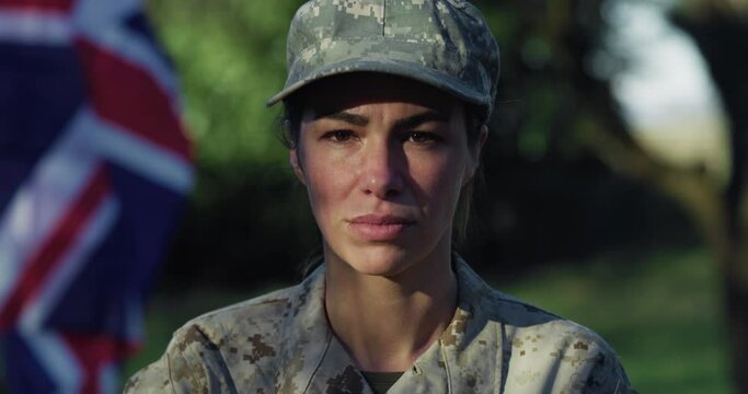 Close Up Slow Motion Portrait of Young Female Patriotic Soldier Standing in front of the British Flag and Looking at the Camera. Devoted Woman in Camouflage Military Uniform Ready to Serve and Defend