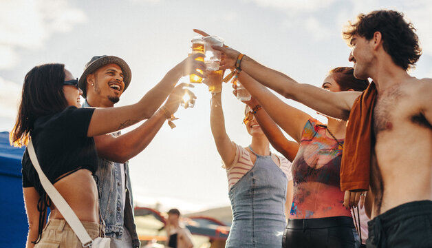 Group of friends making a celebratory toast with beer at a summer festival