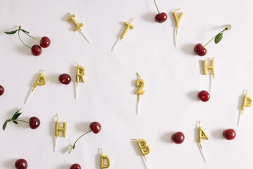 Top view of a gold happy birthday letter candle, number two gold candles for a eighteenth birthday, and cherry disorderly placed. Birthday party ideas.