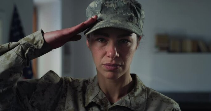 Close Up Portrait of Young Female Patriotic Soldier Looking at the Camera with the U.S. Flag in the Background. Dedicated Woman in Camouflage Military Uniform Saluting, Showing Loyalty to Her Country
