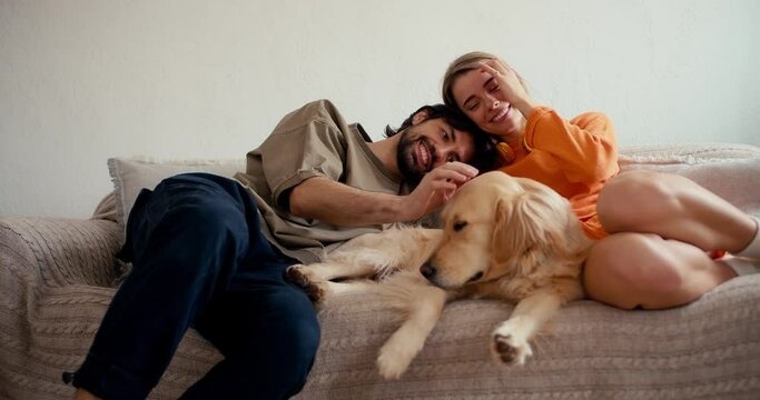 The guy and the girl lie on the couch, stroke their light-colored dog and communicate. Daily life with a pet