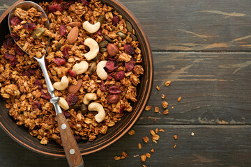 Obraz na płótnie Canvas Homemade granola with greek yogurt or milk and cashews, almonds, pumpkin with dried cranberry seeds in old bowl on dark table background. Healthy energy breakfast or snack. Top view.