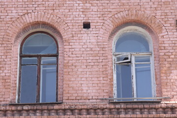 Fototapeta na wymiar Front view of two antique rounded windows against the background of red brick walls, facade of an old house, grunge.