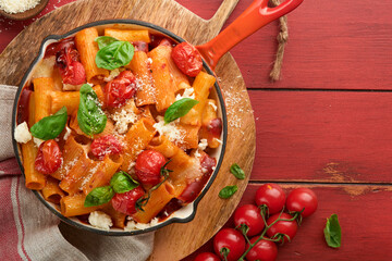 Pasta Tortiglioni with tomato sauce, baked cherry tomatoes, mozzarella and parmesan cheese, basil on old red rustic table. Traditional Italian cuisine. Example Italian food for article. Top view.