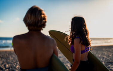 Two surfers with surfboard prepares to hit the waves at sunset.