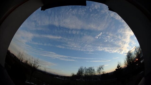 Panorama 204 and time lapse - evening window view with blue sky, moving colorful clouds, moon, sunset and horizon with trees and car traffic with lights on two-lane national road DK1 in Poland.