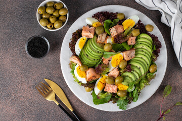 Salad with baked salmon, avocado, eggs and olives, sprinkled with sesame seeds on a white plate