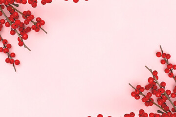 Frame made of branches of red winterberry on a pink background. Place for text.