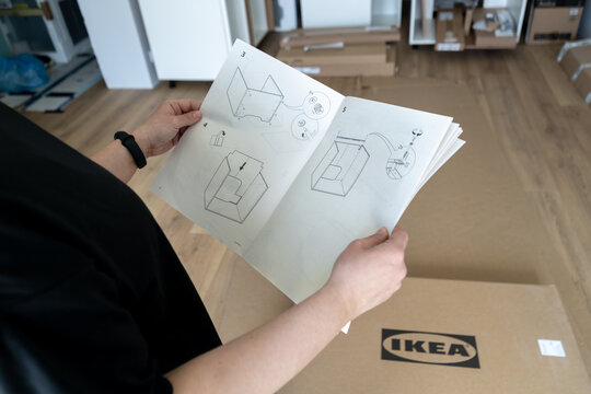 Girl holding IKEA assembly instruction manual of Metod kitchen cabinet. Assembling new furniture from Ikea store at home. Cardboard box package with logo on the floor on June 3, 2023 in Krakow, Poland