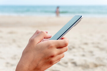 Closeup of hands holding and using smartphone on the beach on vacations. Travel insurance.
Copy space.