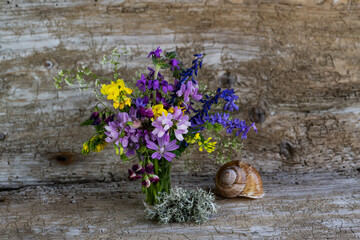 Still life with a bouquet of wildflowers and a snail house.