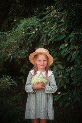 A little beautiful blonde girl in a green dress and a straw hat with a bouquet of hydrangeas