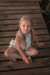 A little blonde girl is sitting on a wooden bridge