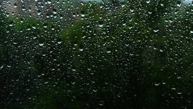 Raindrops on glass on a dark background. Background with rain texture outside the window. Climat is changing. Beautiful summer rain outside the window