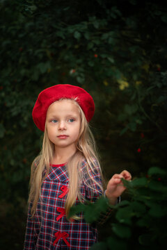 Portrait of a blonde little girl in a red beret and a plaid dress