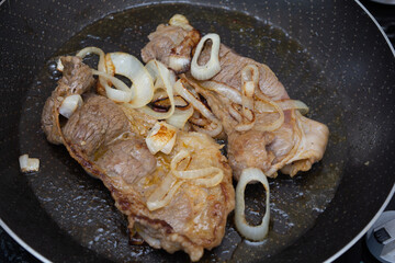 preparing two beef steaks on a frying pan, homemade brazilian cuisine cooking for dinner or lunch with onions..