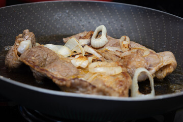 preparing two beef steaks on a frying pan, homemade brazilian cuisine cooking for dinner or lunch with onions..