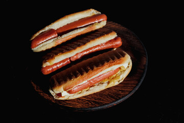 Three delicious, freshly prepared hot dogs displayed on a black wooden stand. Concept for a picnic or barbecue with family and friends. High quality photo