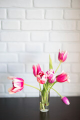Beautiful spring bouquet with pink tulips in a glass vase. Floral still life on the background of a brick wall