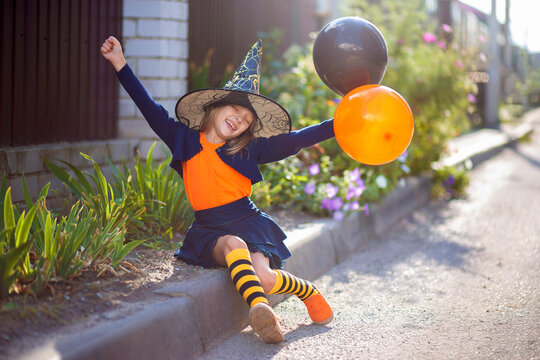 A little girl in a witch costume and with balloons for Halloween walks down the street and rejoices in the holiday