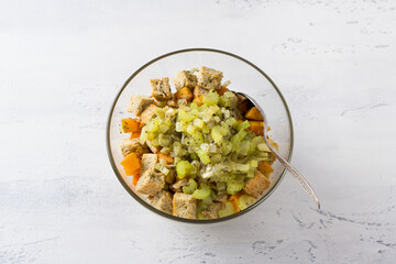 A glass bowl with a mixture of pumpkin cubes, croutons, celery stewed with onions and spices on a light blue background, top view. Stage of cooking delicious homemade casserole