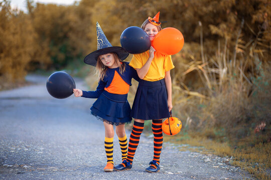 Two girls in Halloween costumes with festive balloons walking down the street. Themed outfit in orange colors for Halloween