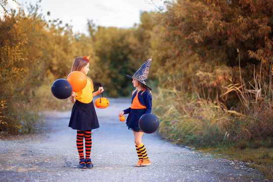 Two girls in Halloween costumes with festive balloons walking down the street. Themed outfit in orange colors for Halloween