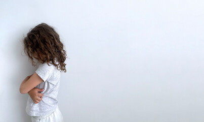 A girl with curly hair, turned away, stands with her head down on a white background.