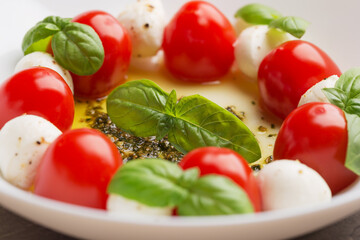 Caprese salad with tomato, mozzarella, basil, olive oil, pesto sauce on white plate close up. Mediterranean cuisine. Focusing on the basil leaves. Macro with shallow dof.