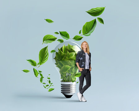 Idea of renewable green eco energy and energy saving. Successful woman is standing near the lightbulb filled with green leaves.