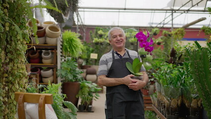 Happy senior Florist holding flower standing inside horticulture store. older male person wearing apron in local business Flower Shop