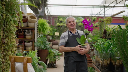 Obraz premium Happy senior Florist holding flower standing inside horticulture store. older male person wearing apron in local business Flower Shop