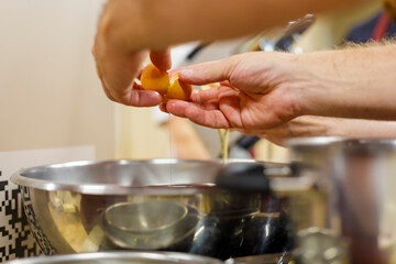 Close-up of the cook's hands cracking a raw egg over a bowl.