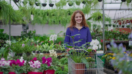 Happy female customer shopping at Flower Shop pushing cart selecting plants and flowers