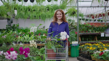 Fototapeta na wymiar Happy female customer shopping at Flower Shop pushing cart selecting plants and flowers