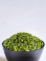 A cup with peeled selected pumpkin seeds on a light background with copy space. Advertising photography for marketplaces.