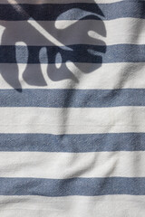 Tropical plants leaf shadow on the blue striped beach towel background