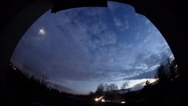 Panorama 204 and time lapse - window evening and night view with dark sky, moving clouds, moon light, horizon with trees, car traffic on national road DK1 with lights of passing cars in Poland.