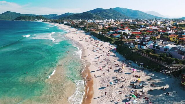 Aerial view of the sea with gentle waves and sandy beach with people relaxing on it. Lomba do Sabao beach on Santa Catarina island in Brazil