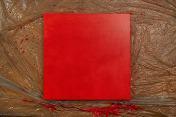 Small square canvas painted red with thin plastic underneath. 