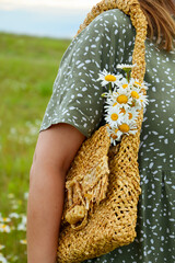 A young woman in a dress is holding a straw bag with a bouquet of daisies. Happy lady and nature - the concept of harmony. The idea of self-care, healthy lifestyle and positive