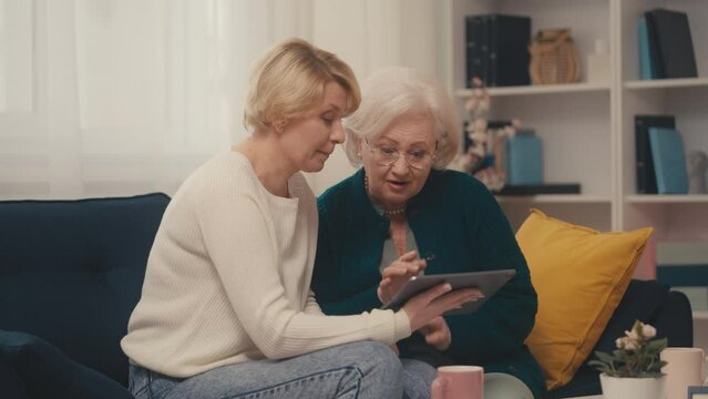 Mother and adult daughter looking at family photos using tablet, family memories